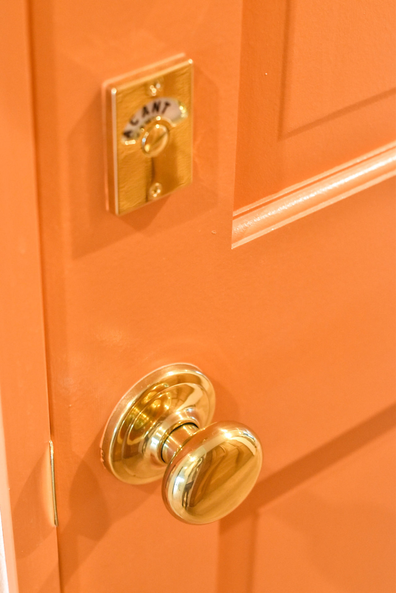 オレンジ色の扉とゴールドのドアノブと表示錠
