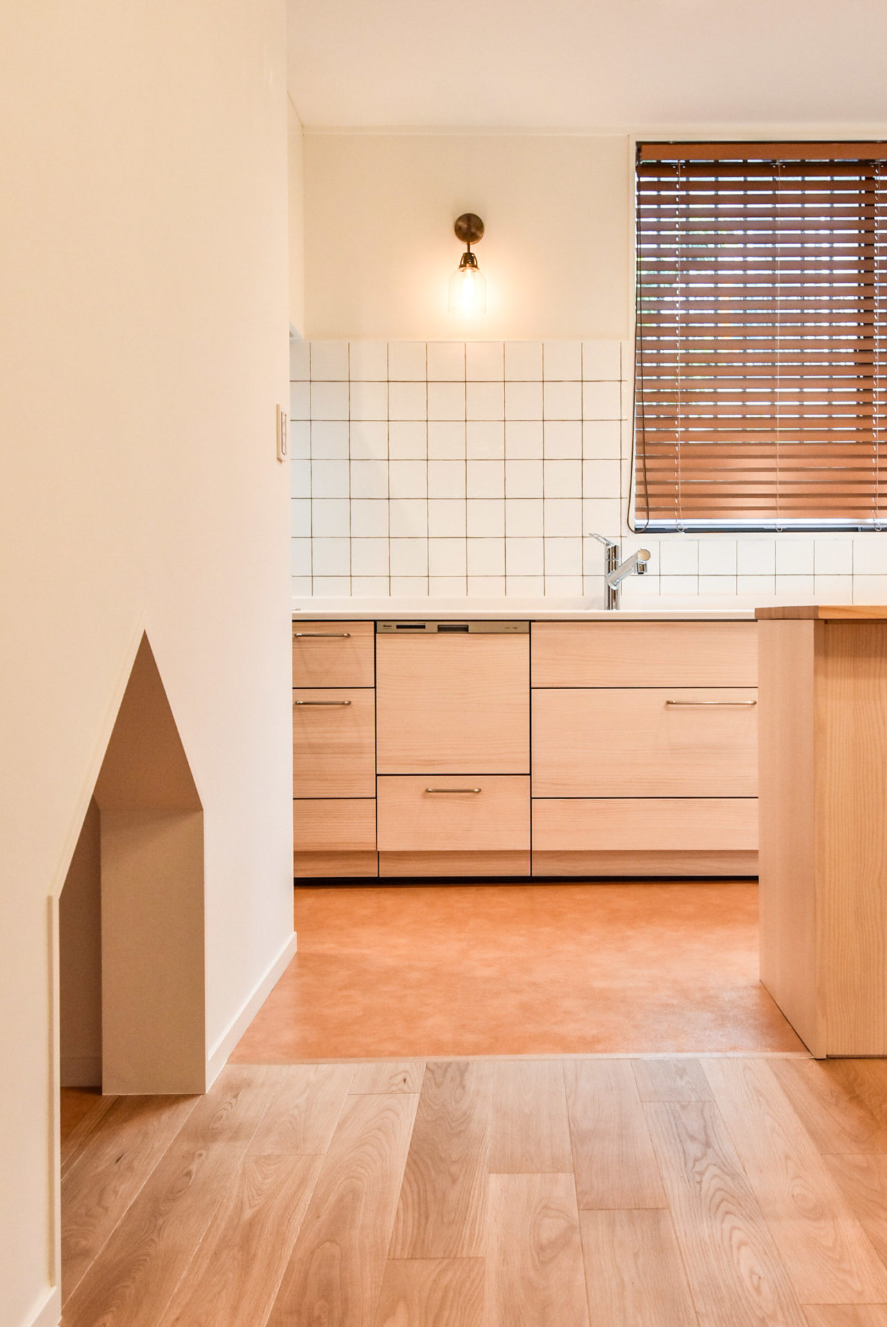 白いタイル貼りの壁のキッチンと家型開口のワンちゃん用のスペース