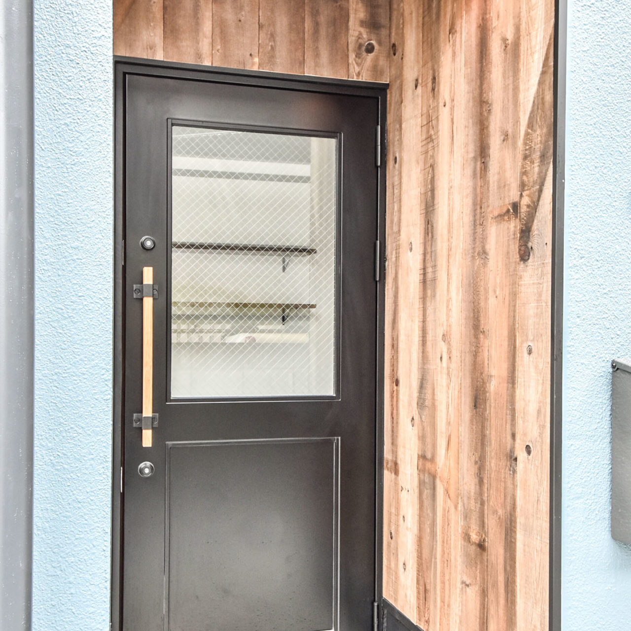 木板貼りの壁と黒い扉のある玄関ポーチ
