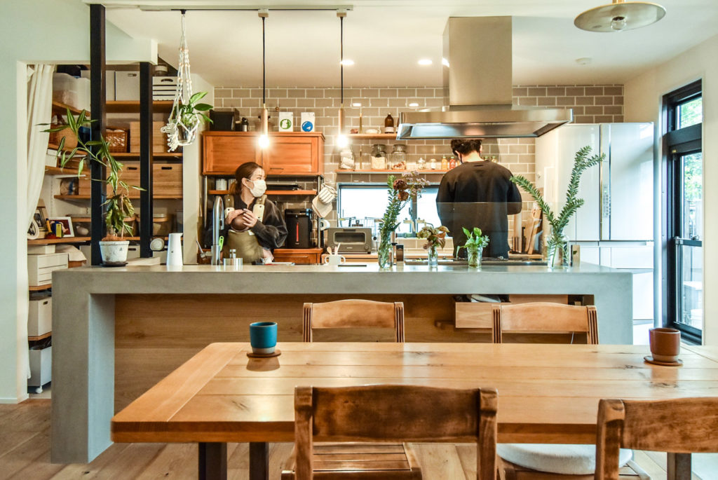 モルタルのアイランドキッチンと木製のダイニングテーブル