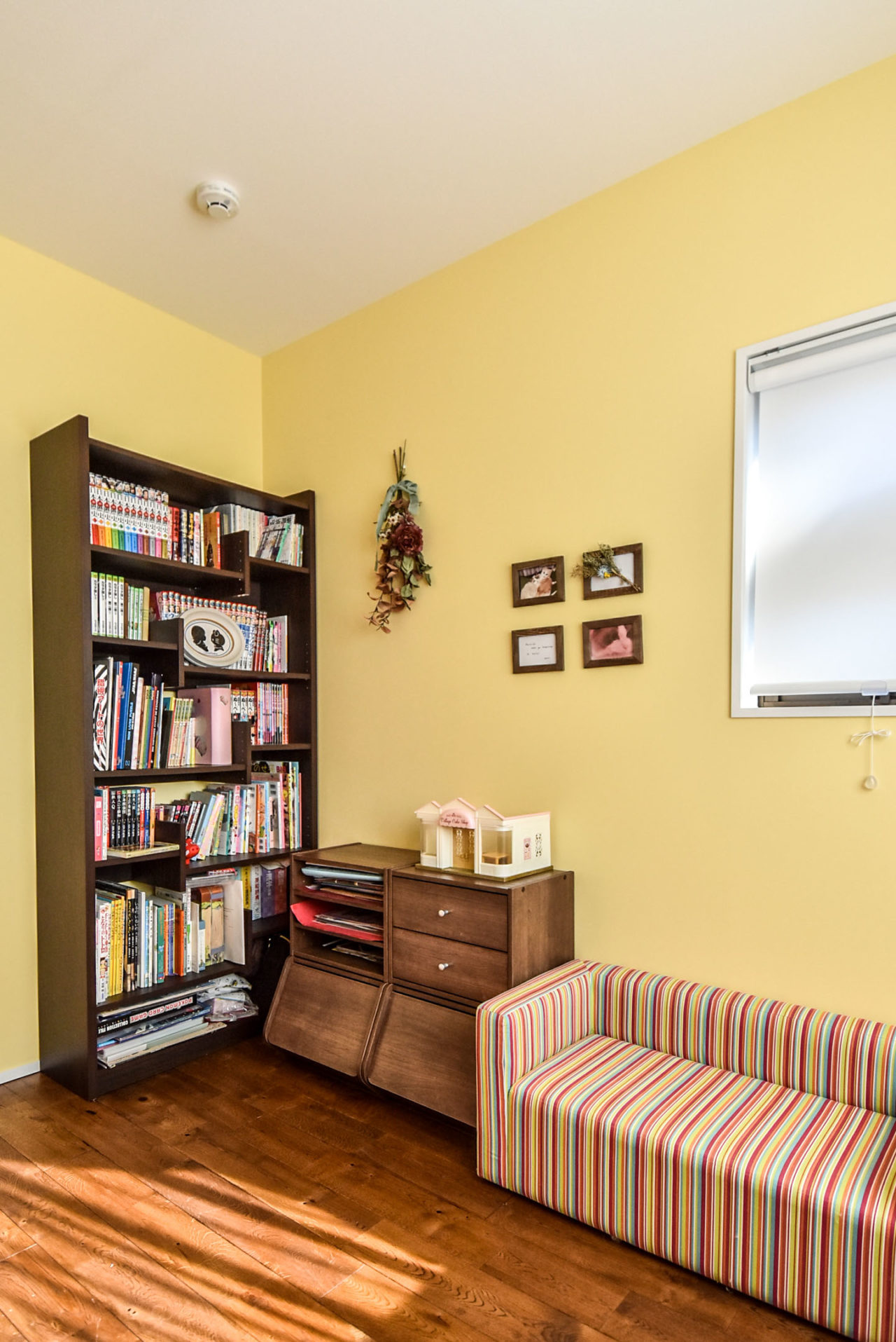 黄色のアクセントウォールの部屋と本棚とソファ