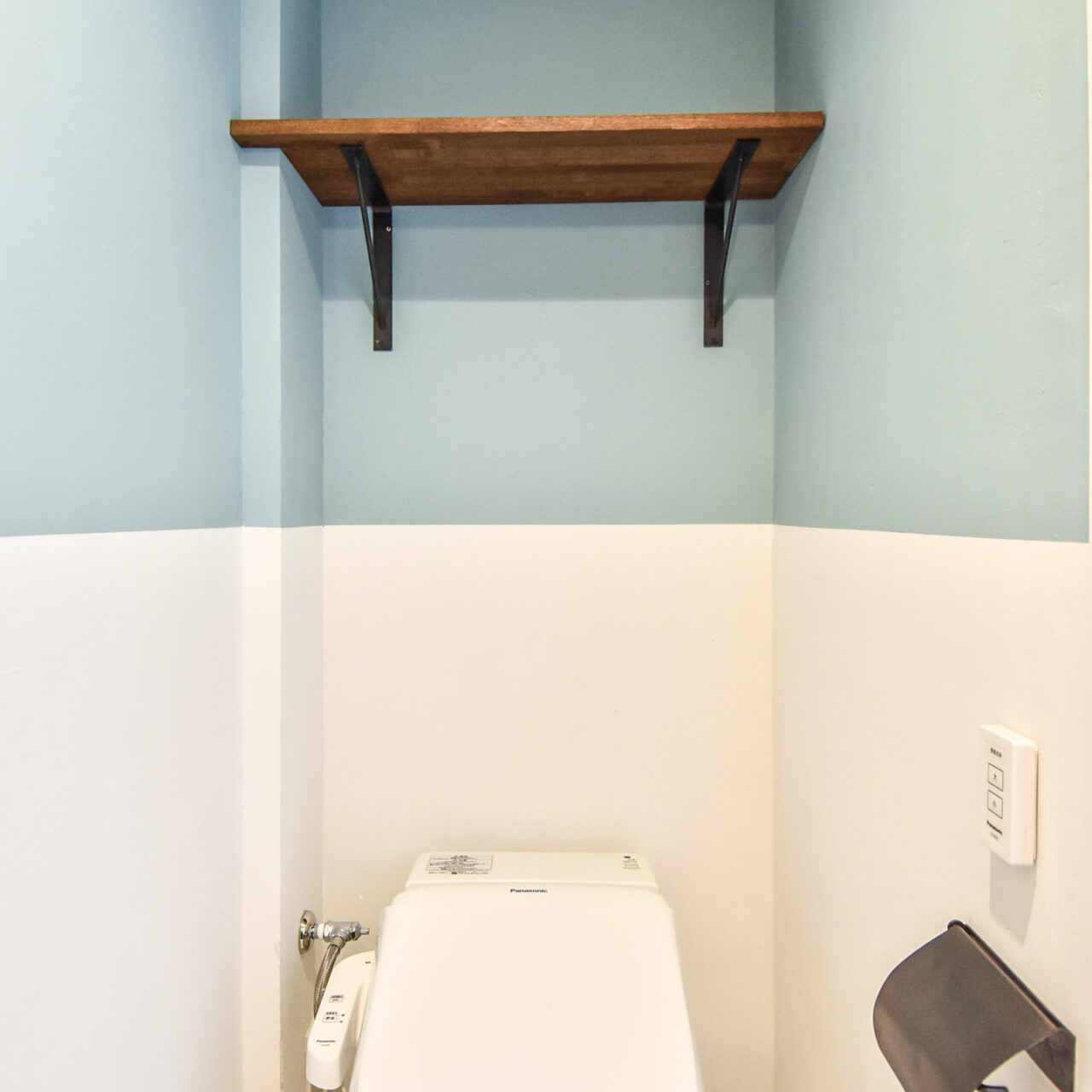 ツートーンの壁と木製棚のあるトイレ