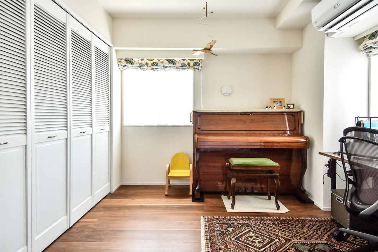 木製のアップライトピアノとルーバー折戸のある寝室