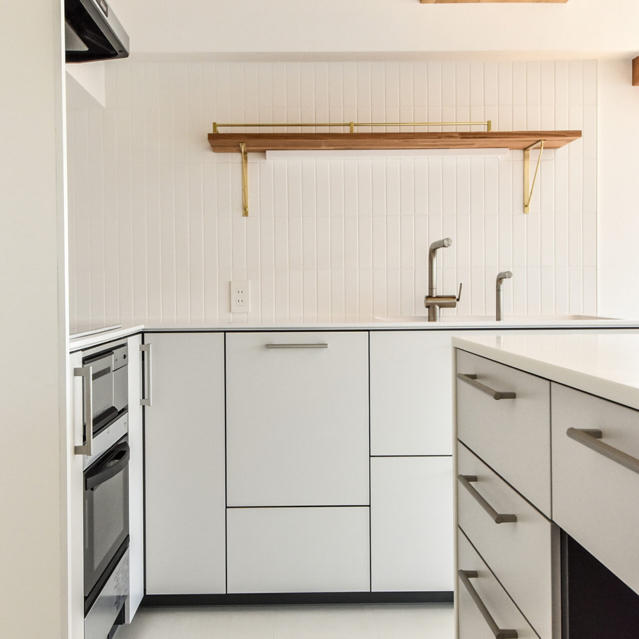 白の扉とタイルと真鍮金物の棚のあるキッチン