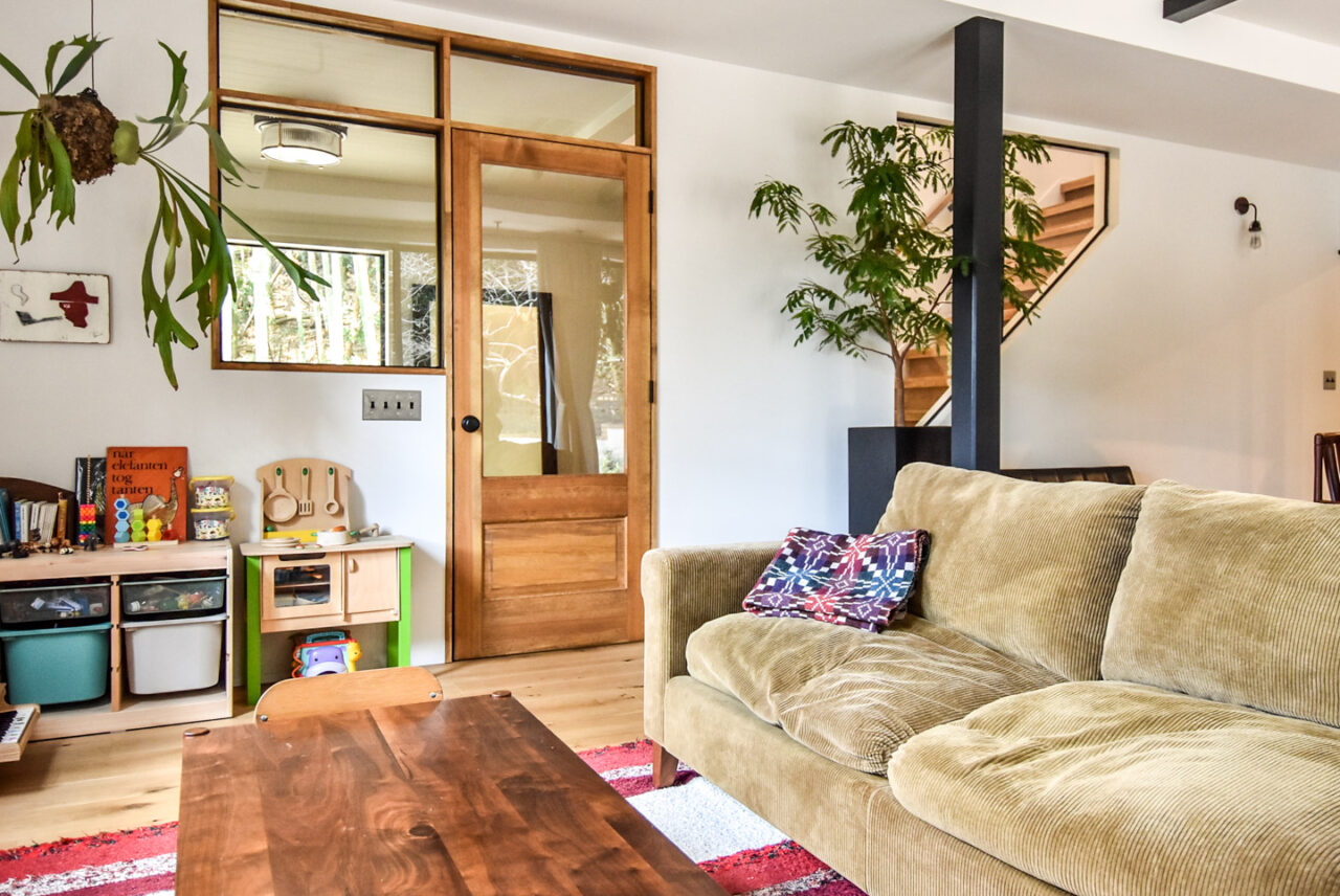 大きな木製室内窓とソファのあるリビングスペース