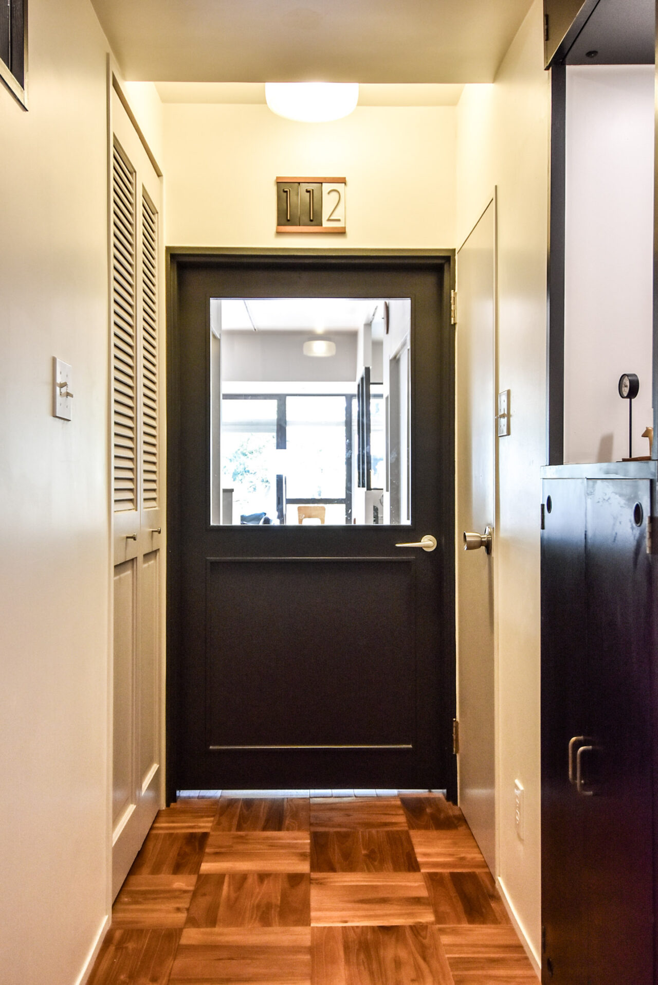 部屋番号112の表示がある、明るく清潔な廊下に位置する黒いドア。ドアの窓からは、室内が一部見えています。