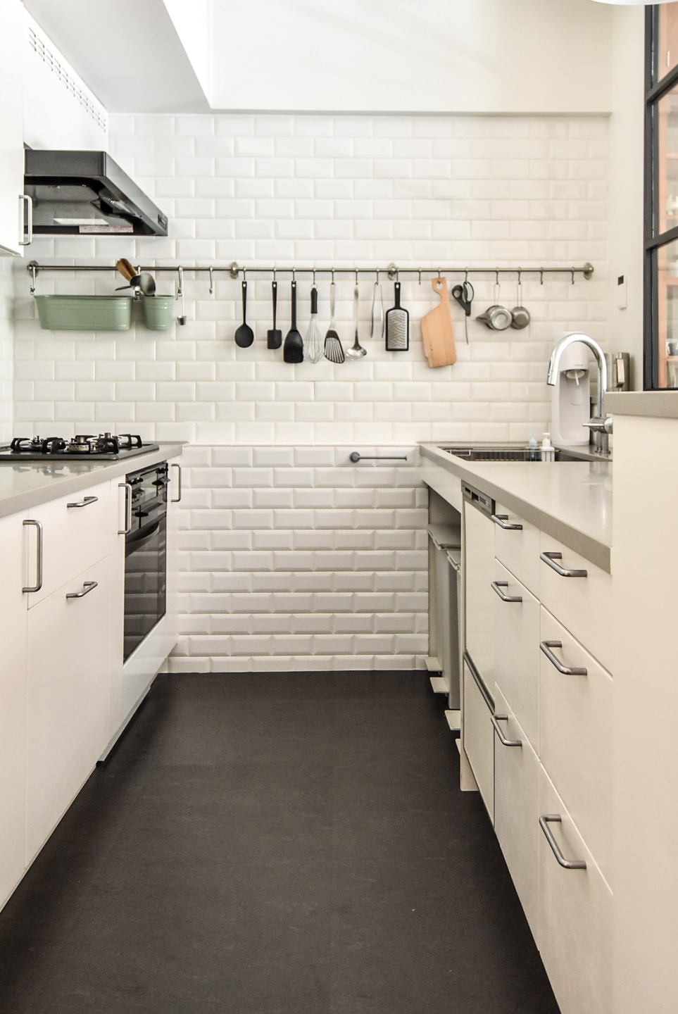 モダンで明るいキッチン、白いタイルの壁、ステンレス製の調理器具が並ぶ。シンプルで機能的なデザインが特徴。