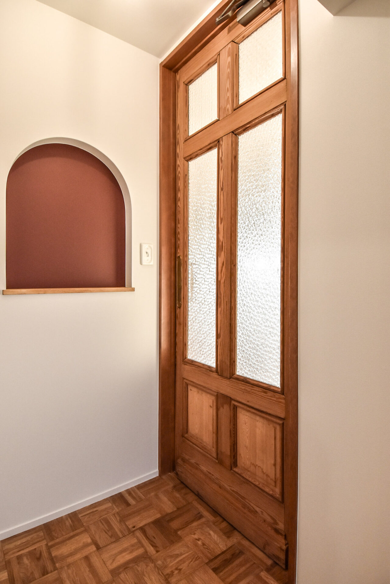アーチ型の壁のニッチにあるピンクのアクセントと木製フレームのドア
