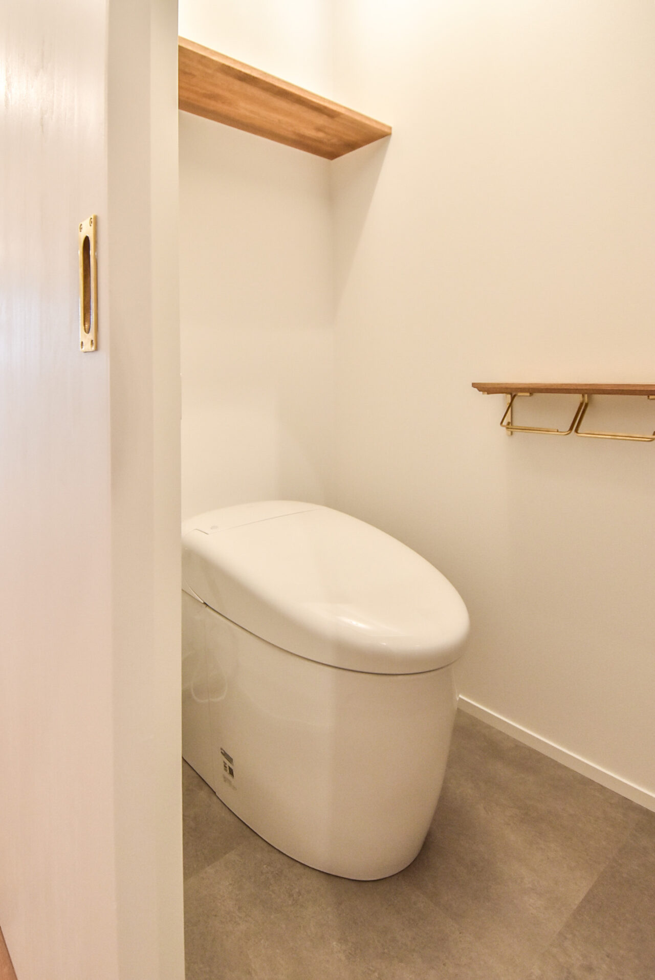 白い壁とモダンなトイレ、木製のシェルフがあるシンプルなレストルーム