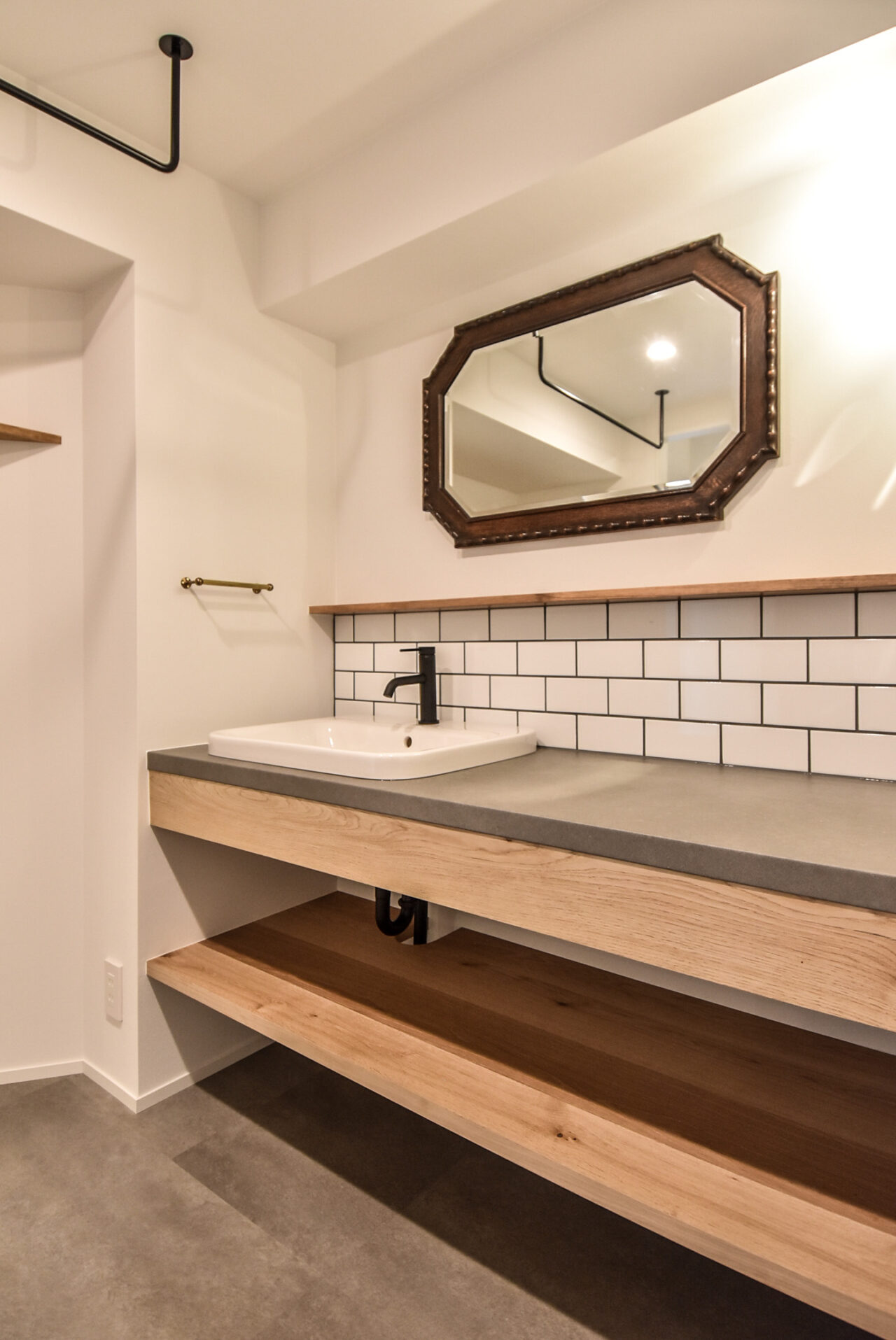 白い壁とヘキサゴンミラー、下部に木製シェルフがあるモダンな洗面スペース