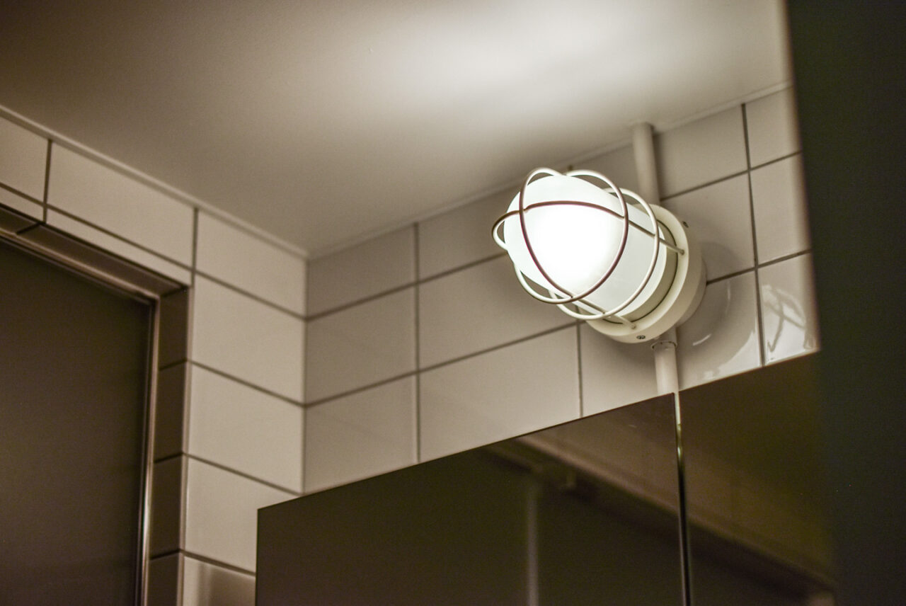 バスルームの天井に取り付けられた丸いライト。白いタイルと鏡が背景です。明るくて清潔な印象を与えます。