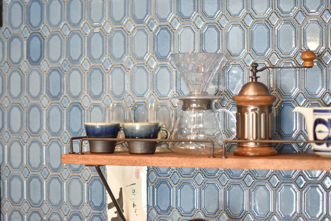 キッチンの棚に並べられたコーヒーセットと青いタイルの壁。