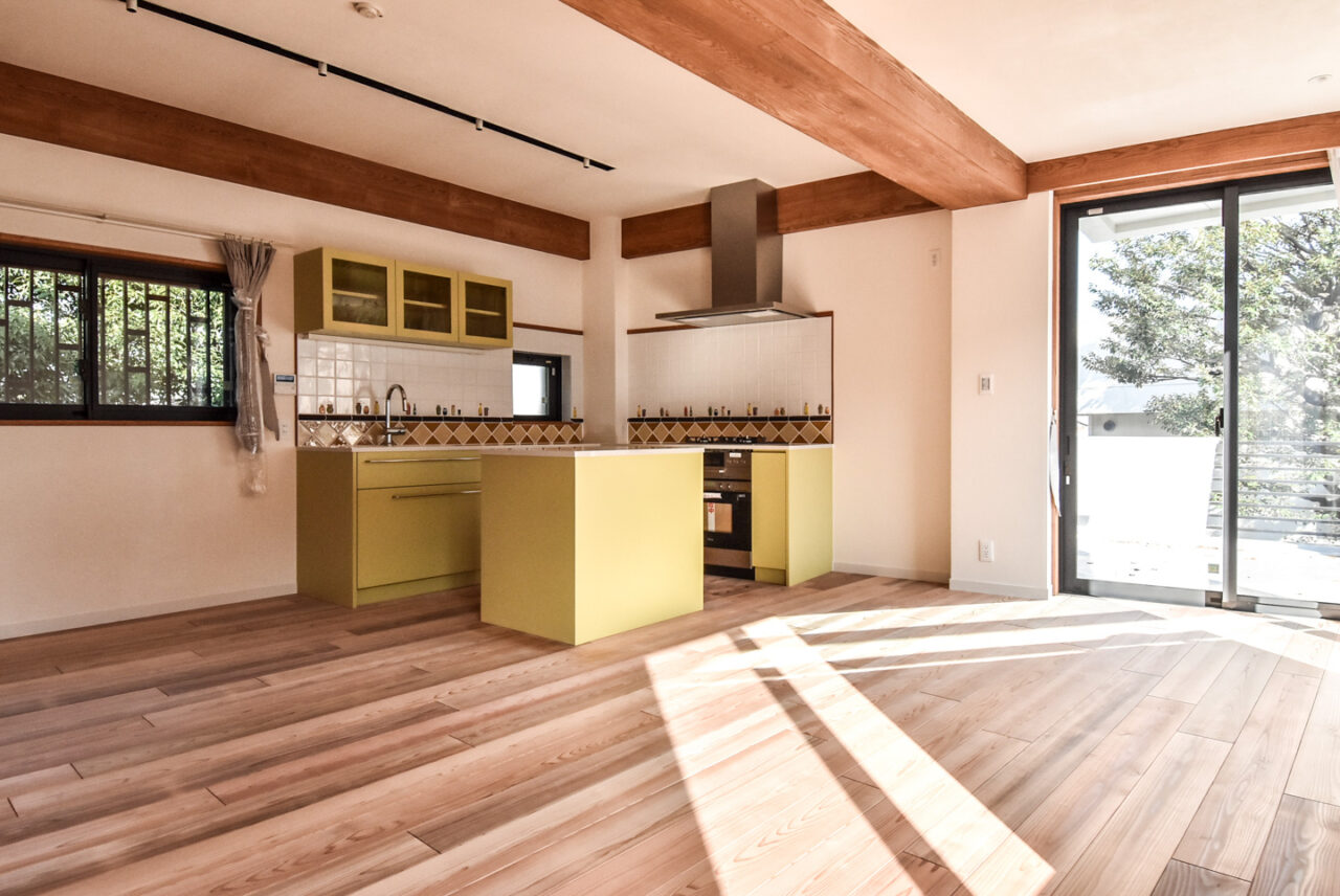 日光が差し込む広々としたキッチンには、モダンな黄緑色のキャビネットとステンレスの調理器具があり、天井には木製の梁が特徴的です。