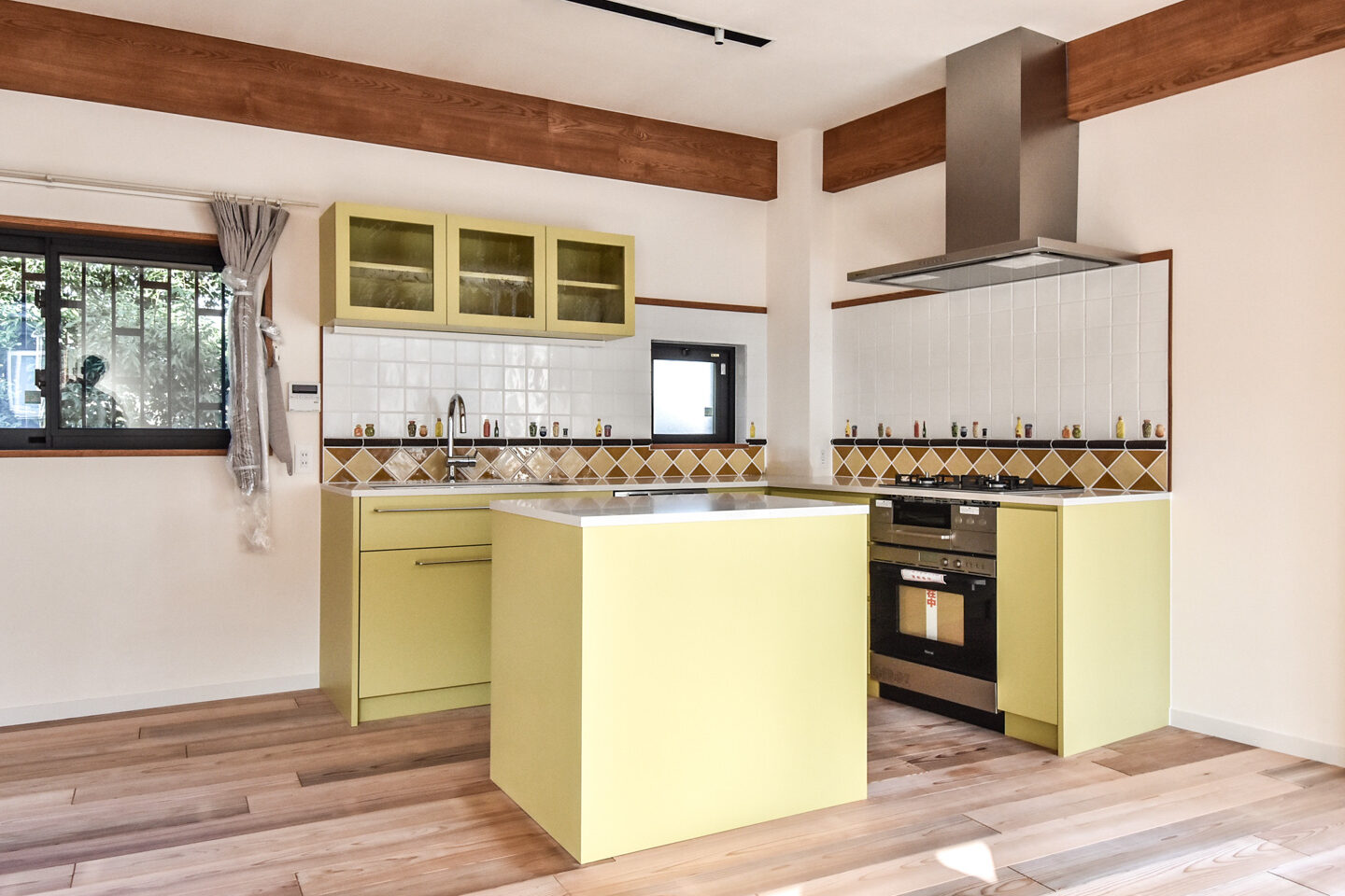 明るい光が降り注ぐキッチン、中央には黄緑色のアイランドカウンターと白いタイルの壁