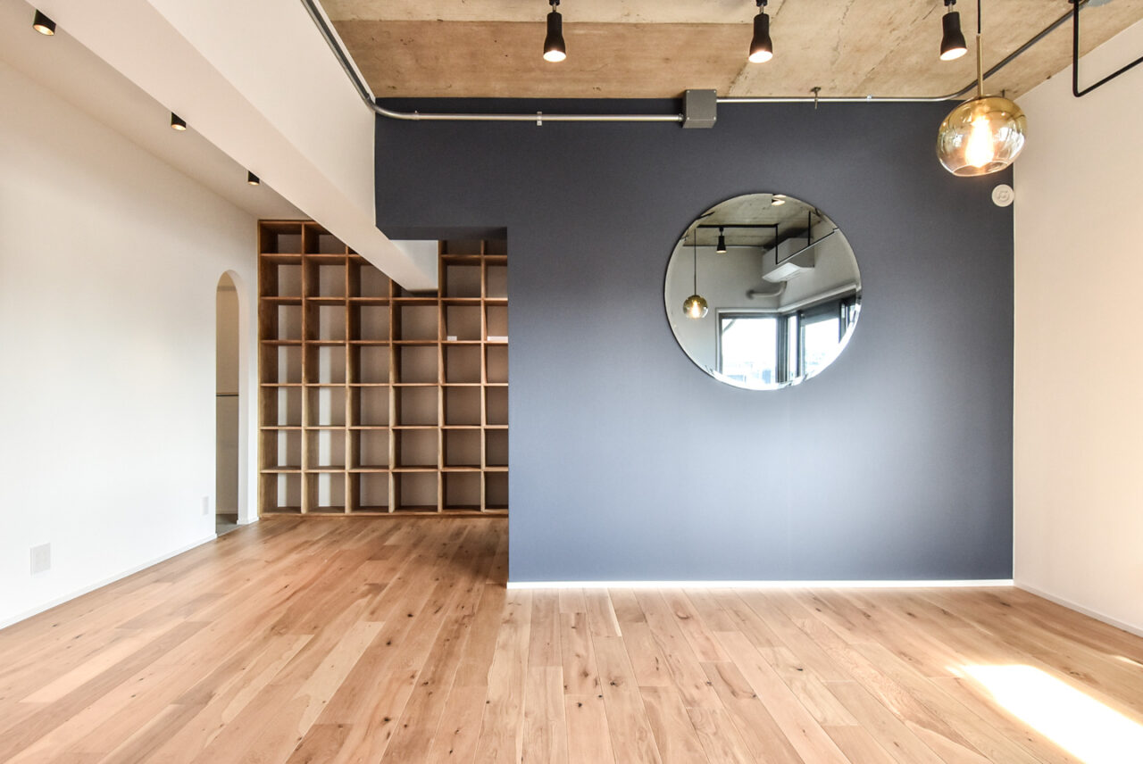 木製の床板とシンプルな本棚、中央に円形のミラーがある壁。