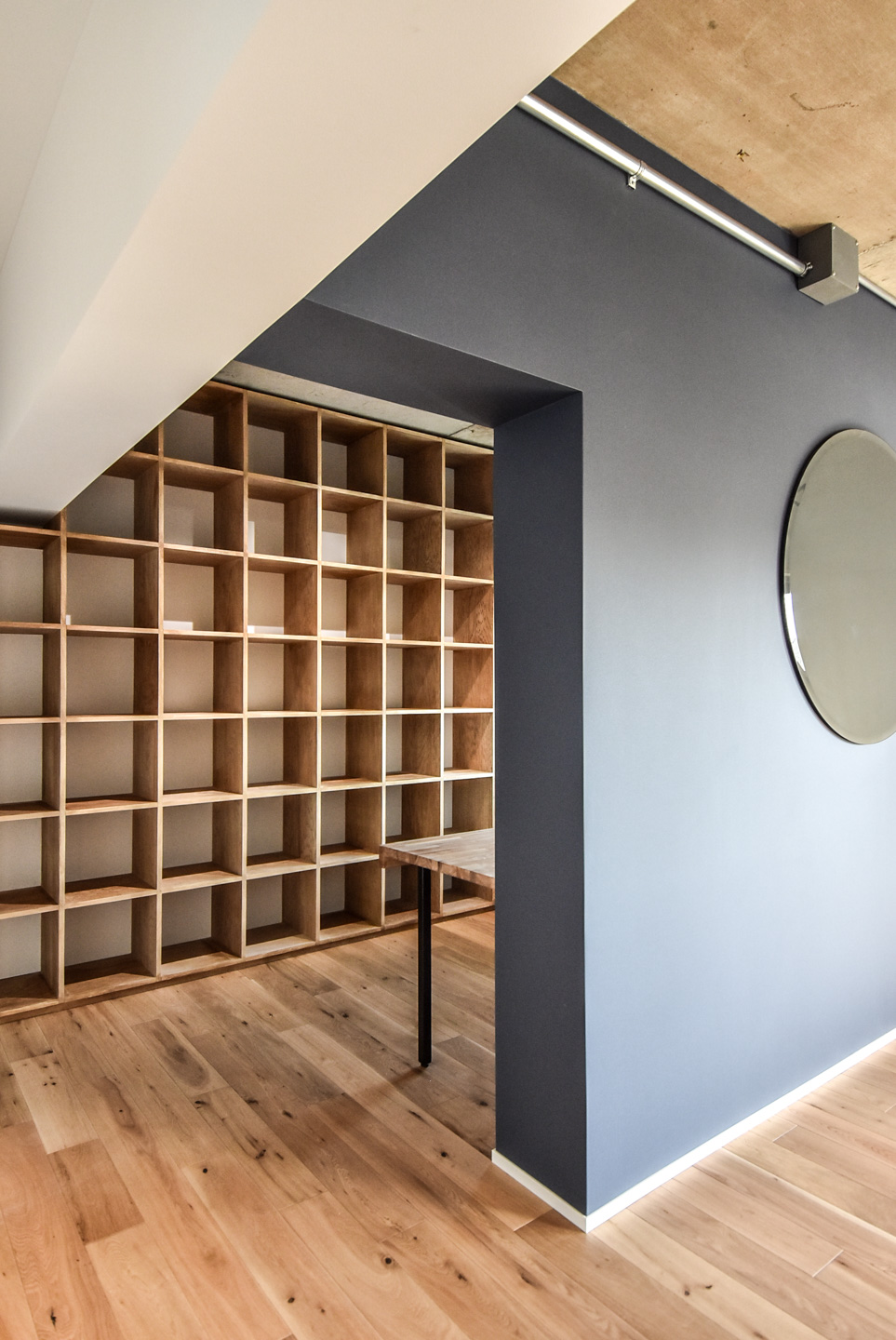 木製の床板とシンプルな本棚、中央に円形のミラーがある壁。