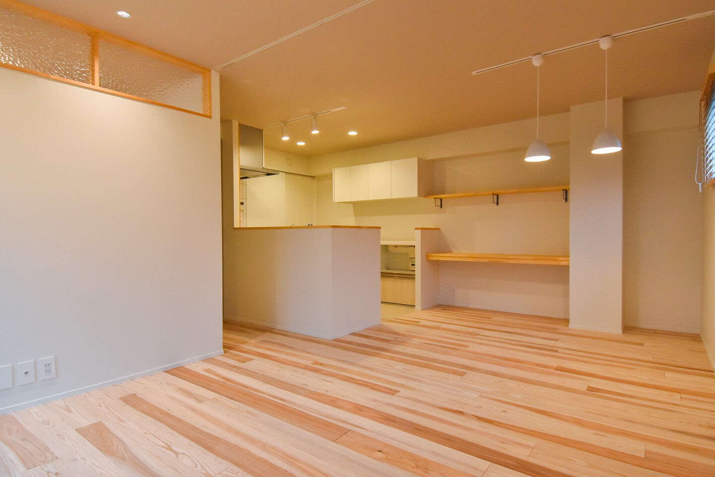 キッチンとリビングルームが一体となったオープンプランの空間。木製の床と棚がナチュラルな雰囲気を引き立てています。