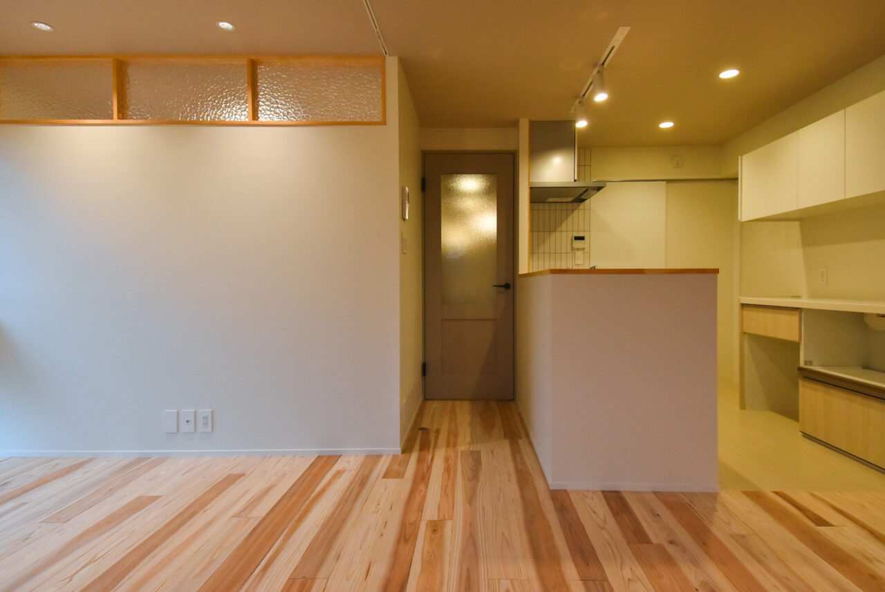 リビングルームからキッチンを眺めた風景。シンプルなデザインのドアと白い壁が空間を明るくしています。