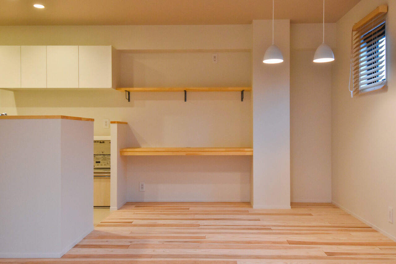 木製のカウンターと棚を備えたオープンプランのキッチン。明るい照明が作業スペースを照らしています。