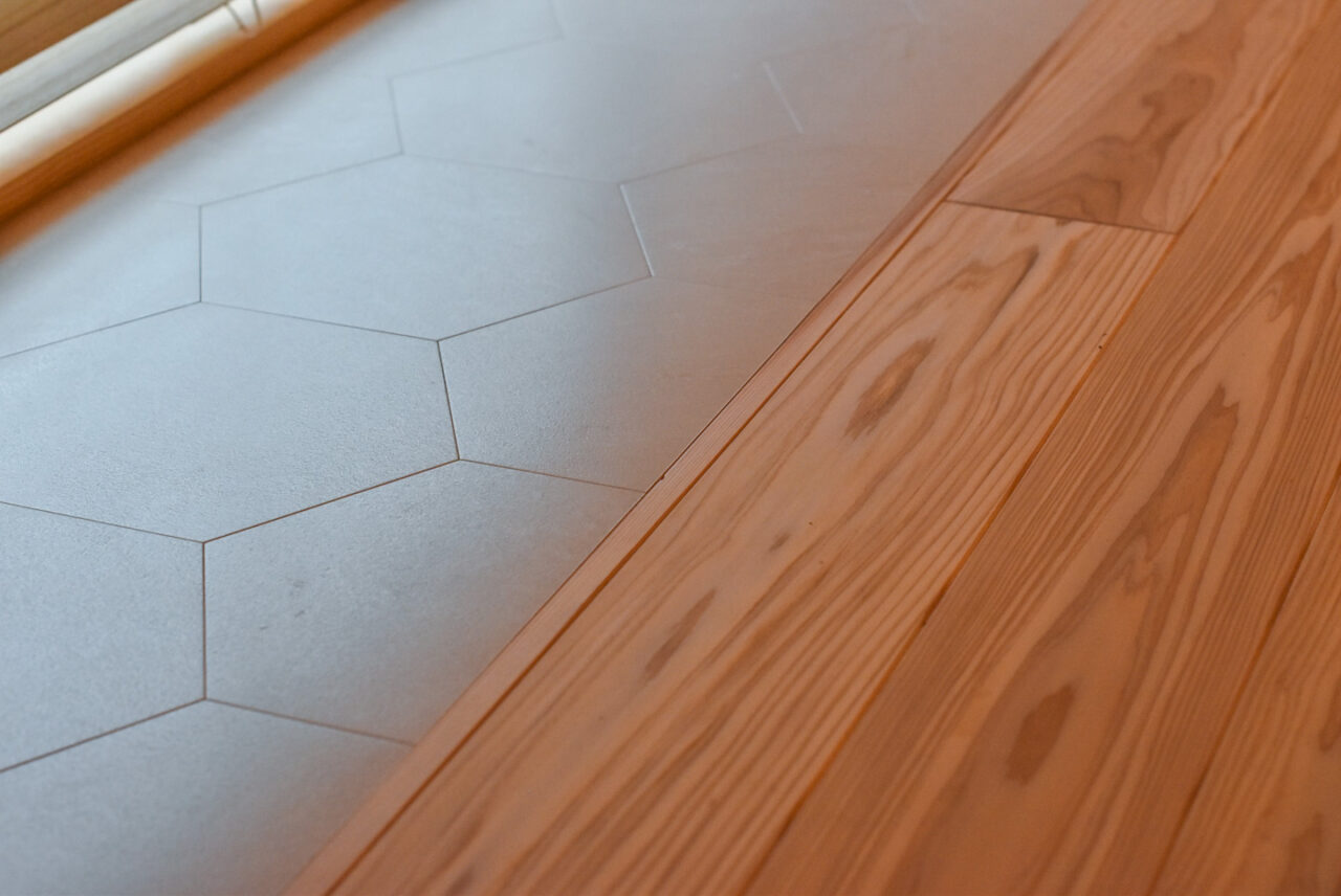 六角形の白いタイルと木製フローリングが接する床のクローズアップ。モダンなデザインの空間を演出しています。