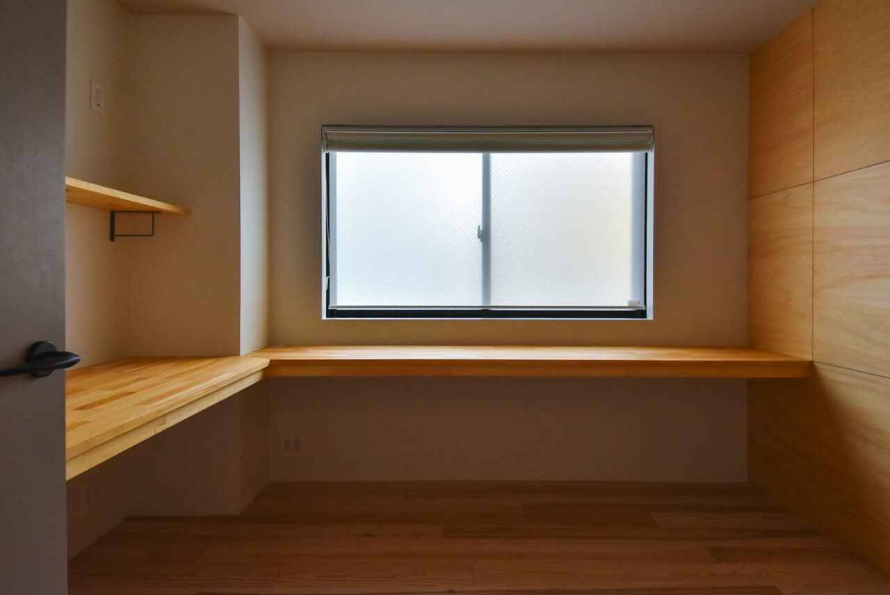 窓際に設置された広々とした木製のカウンターデスクが特徴的な部屋。シンプルで機能的なデザインです。